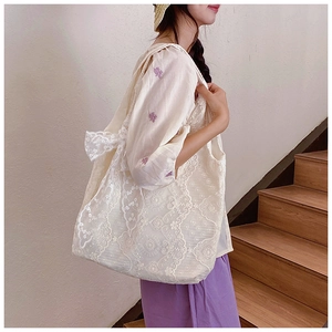 Detail of white lace tote bag with floral embroidery and side bow on a female model