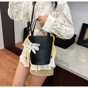 Detail of black matte leather bucket bag featuring a large white flower charm and yellow drawstrings