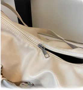 Detail shot of smooth metal zipper on a cream-colored pleated tote bag made of PU leather