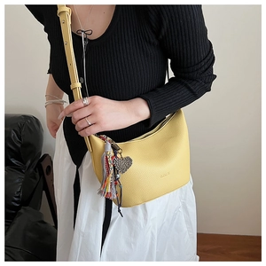 Détail du sac hobo en cuir jaune avec pompon tissé et breloque en forme de cœur