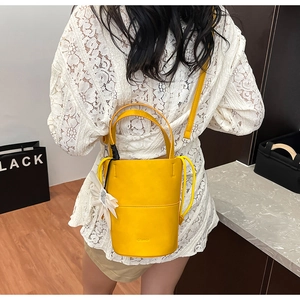 Detail of a bright yellow bucket bag with double handles and a white flower charm accessory