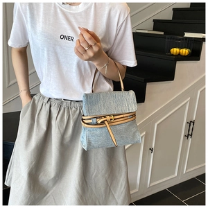 Detailed view of light blue denim handbag featuring a stylish camel leather belt detail