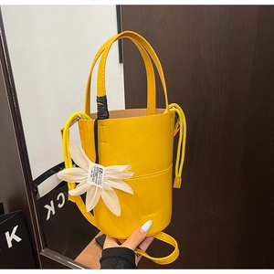 Detailed view of yellow bucket bag with floral charm and adjustable shoulder strap