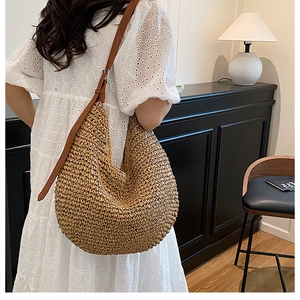 Detailed close-up of woven straw texture and premium brown leather shoulder strap on beach bag