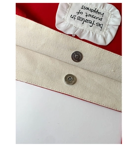 Detail of red canvas tote bag with magnetic clasp, beige lining, and ruffled trim
