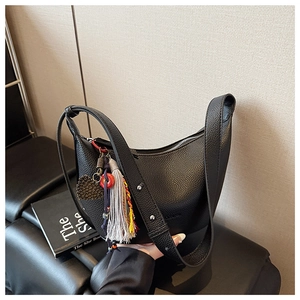 Détail d'un sac en cuir grainé noir avec des pompons colorés et des breloques