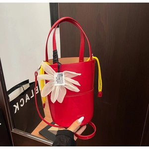 Detail of red bucket bag featuring a large white flower charm and yellow drawstring closure