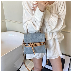 Detail of blue denim crossbody bag with brown leather strap worn by a model in white