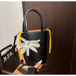 Close-up of black leather bucket bag with white floral charm and yellow drawstring details