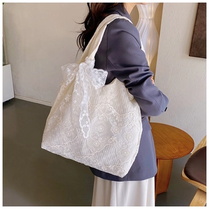 Detailed shot of white floral lace tote bag with large decorative bow on model's shoulder
