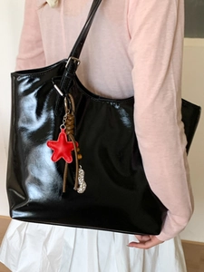 Grand sac cabas noir brillant en cuir verni avec pendentif étoile rouge porté par mannequin