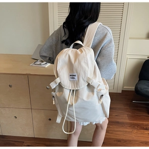 Vue détaillée du sac à dos blanc crème avec fermeture à rabat et cordons de serrage