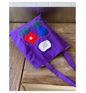 Detail of purple canvas tote bag featuring floral appliques and a decorative woven label