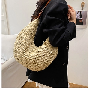 Detail of a beige woven straw shoulder bag with brown leather strap worn by a model