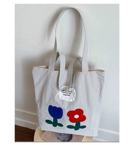 Detail of canvas tote bag showing blue floral embroidery and white woven patch on the side