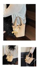 Detalle de bolso cubo beige con grabado de lichi, cierre de metal y colgante oso
