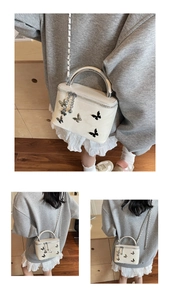 Close-up of cream box bag with metallic butterfly details and silver chain strap