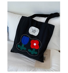 Close-up of black canvas tote bag featuring floral embroidery and ruffle text patch