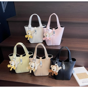Detalle de cinco bolsos cubo en varios colores con cierre de metal y colgante de oso