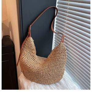Detailed view of woven straw texture and brown leather strap on a crescent hobo bag