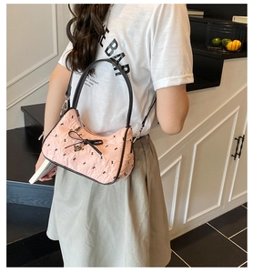 Detailed close-up of a pink pleated shoulder bag with black bow and gold heart charm detail