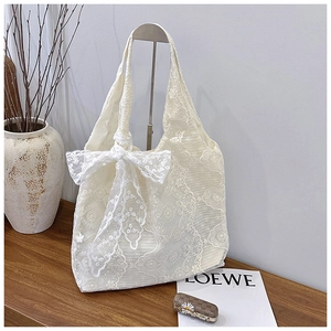 Detail of white lace tote bag featuring intricate floral patterns and a large bow decoration