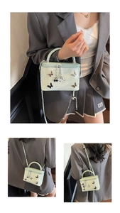 Close-up of light green patent leather box bag featuring 3D butterfly charms and chain