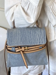 Light blue denim handbag with brown leather strap and gold buckle in a minimalist style