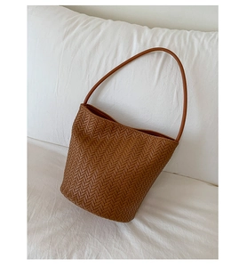 Detail of brown woven leather tote showing V-shaped herringbone texture and shoulder strap