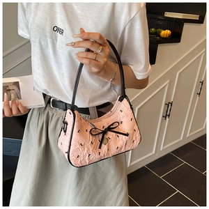 Detail of pink pleated underarm bag featuring a black silk bow and gold heart pendant