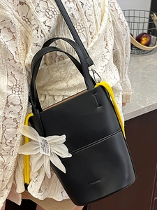 Chic black bucket bag with white floral charm and yellow cord details for women