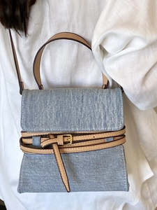 Blue denim crossbody bag with brown leather trim and decorative buckle detail