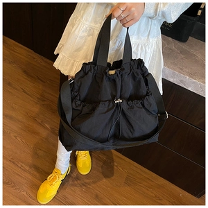 Detail of black drawstring tote bag with textured nylon fabric and functional pleated pockets