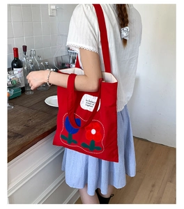 Red canvas tote bag with tulip embroidery and broad shoulder strap in a modern setting