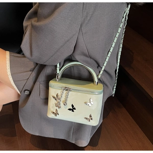Green box bag featuring silver butterfly accents worn by a model in a grey suit