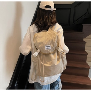 Détail du sac à dos en nylon beige avec cordon de serrage et boucle blanche sur un escalier