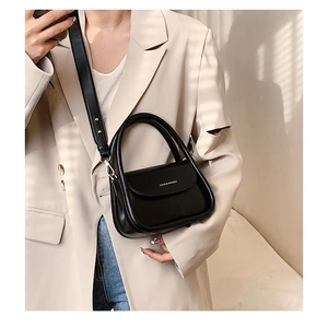 Close-up of black crossbody square bag detail with logo and textured leather surface
