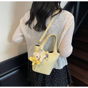 Detalle de bolso tipo cubo amarillo pálido con textura lichi y colgante de osito suave