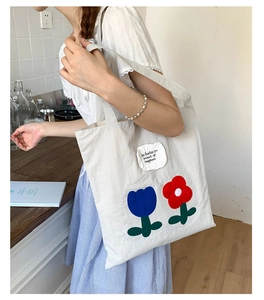 Close-up of white canvas tote bag with floral tulip embroidery and minimalist lettering