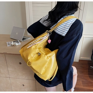 Detail of yellow pleated tote bag with heart pendant and drawstring on a model