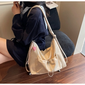 Detail of beige pleated tote bag with drawstring pocket and a pink heart charm