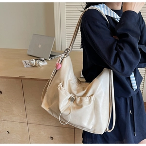 Detail of cream white hobo bag with drawstring pocket and decorative heart pendant accessory