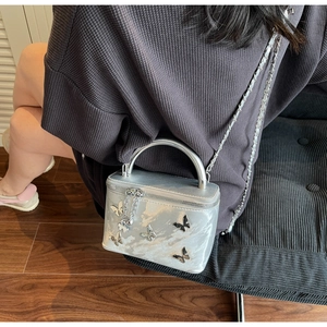 Detail of silver glitter box bag with butterfly charms and metal chain strap on a model