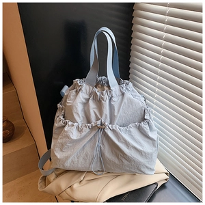 Detail view of light blue nylon drawstring tote bag on beige coat with soft shadows