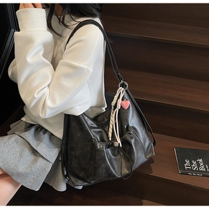 Detail of a large black leather tote bag featuring pleated pockets and heart charms