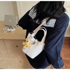 Detalle del bolso de cubo blanco en cuero granulado con colgante de oso amarillo en mesa