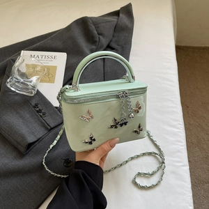 Detail of mint green box vanity bag with silver butterfly charms and chain strap