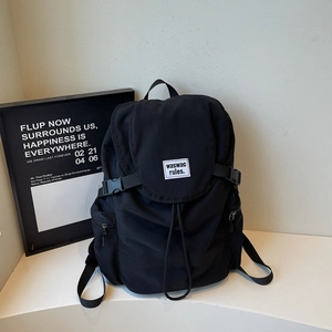 Détail du sac à dos en nylon noir montrant le rabat, la boucle et l'étiquette tissée