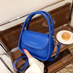 Blue matte leather handbag with double handles and fashion lettering shown on a chair