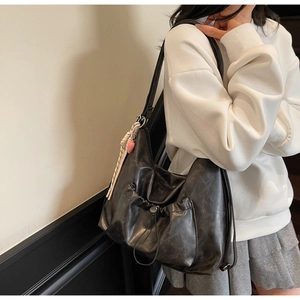 Detail shot of black faux leather tote with drawstring pocket and heart charm on model